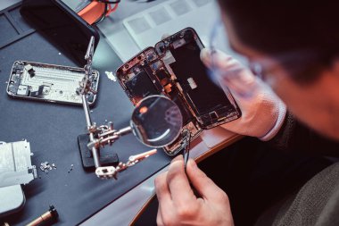 Tamirci hasarlı smartphone onarmak için Büyüteç'i ve cımbız kullanır.