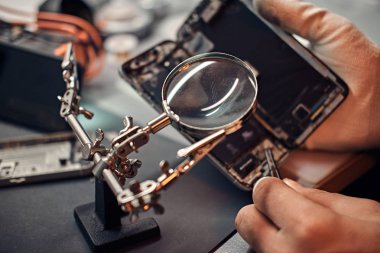 Tamirci hasarlı smartphone onarmak için Büyüteç'i ve cımbız kullanır.