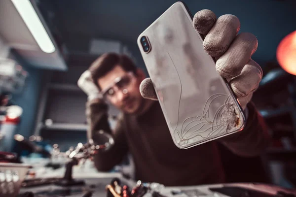 Técnico eletrônico mostrando um smartphone com um corpo quebrado em uma oficina — Fotografia de Stock