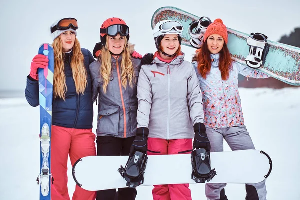 Веселі жінки друзі в спортивному зимовому одязі зі сноубордами і позує на лижах — стокове фото