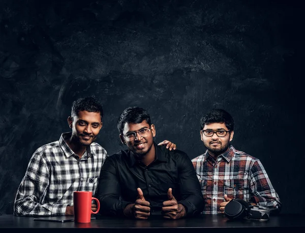 Drie donkere guy poseren zitten aan de tafel duimen omhoog tillen — Stockfoto