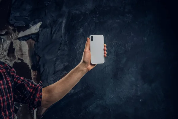 Новый современный смартфон с красивым дизайном в руках человека на фоне темной стены — стоковое фото