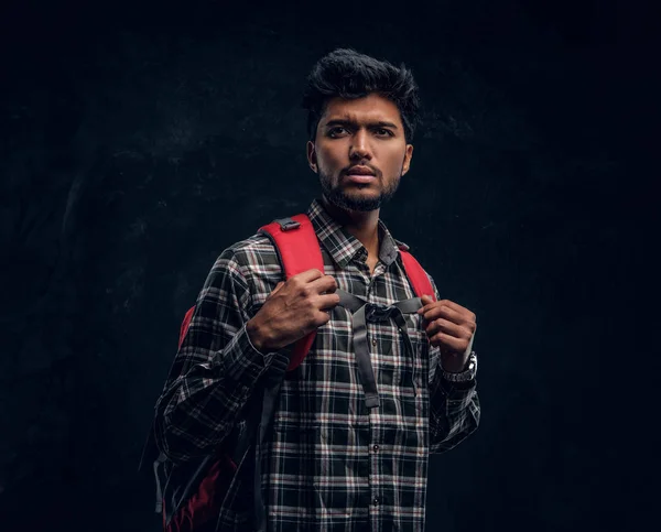 Hint öğrenci bir ekose gömlek giymiş bir sırt çantası ile. Studio fotoğraf bir karanlık dokulu duvara — Stok fotoğraf