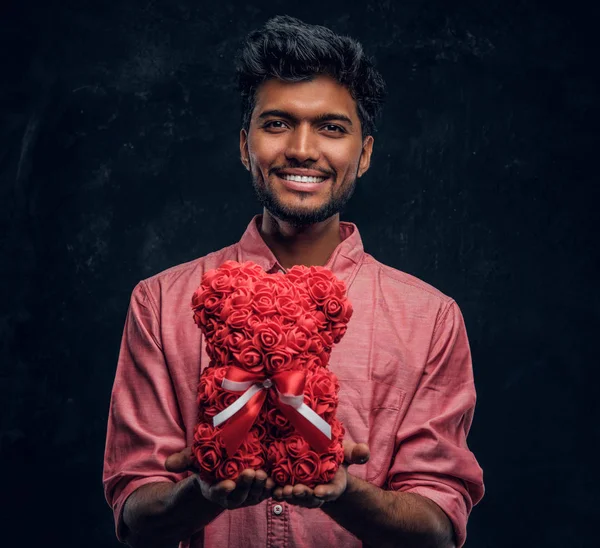 Indiano cara em uma camisa rosa detém um belo presente, sorrindo e olhando para a câmera. Humor romântico, relação amorosa . — Fotografia de Stock