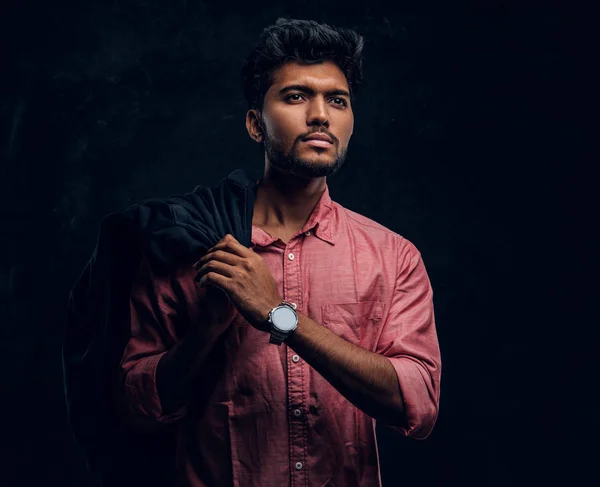 Vogue, fashion, style. Handsome young Indian guy wearing a pink shirt holding a jacket on his shoulder and looking sideways.