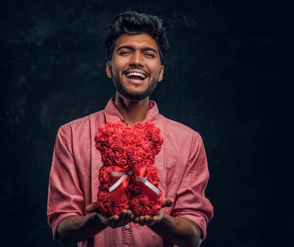 Indiano cara em uma camisa rosa detém um belo presente, sorrindo e olhando para a câmera. Humor romântico, relação amorosa . — Fotografia de Stock