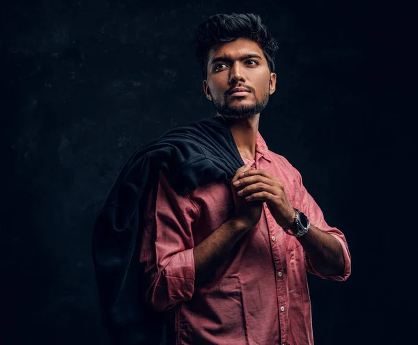Vogue, fashion, style. Handsome young Indian guy wearing a pink shirt holding a jacket on his shoulder and looking sideways.