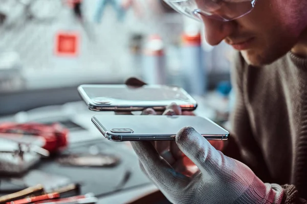 Técnico detém dois smartphones idênticos para comparação, em uma mão quebrada e em outra nova — Fotografia de Stock