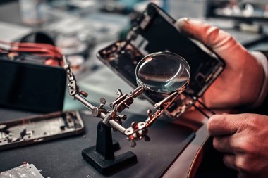 Tamirci hasarlı smartphone onarmak için Büyüteç'i ve cımbız kullanır.