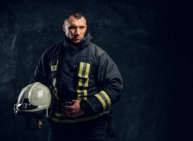 Üniformalı bir kask tutarak kendine güvenen itfaiyeci ve kameraya doğru görünüyor