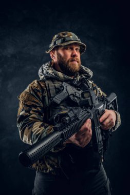 Special forces soldier in the military camouflaged uniform holding an assault rifle. Studio photo against a dark textured wall clipart
