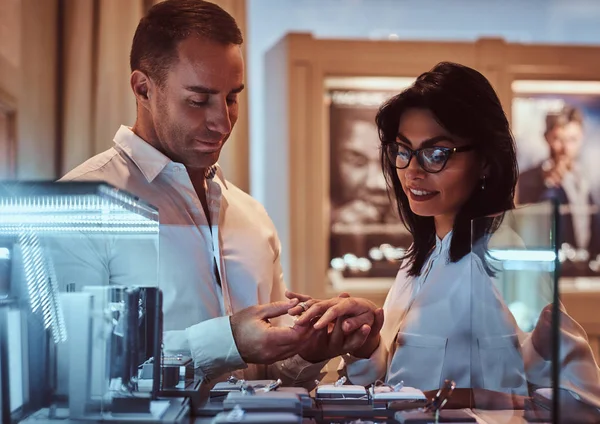 Elegantly dressed man trying on the wedding ring on the hand of his girlfriend in a jewelry store