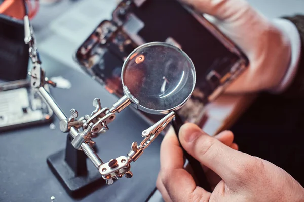 Opravář používá lupy a pinzety k opravě poškozené smartphone. — Stock fotografie