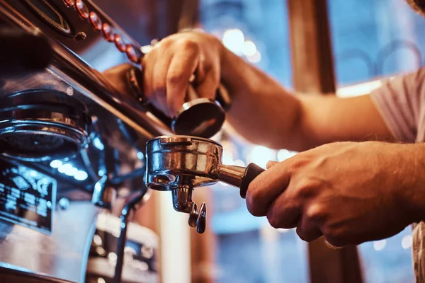 Foto de un barista sosteniendo un portafilter con un café negro molido y trabajando en una máquina de café en una cafetería o restaurante —  Fotos de Stock