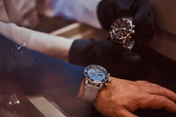 Assistente aiuta il cliente a provare esclusivi orologi da uomo, mani close-up . — Foto Stock