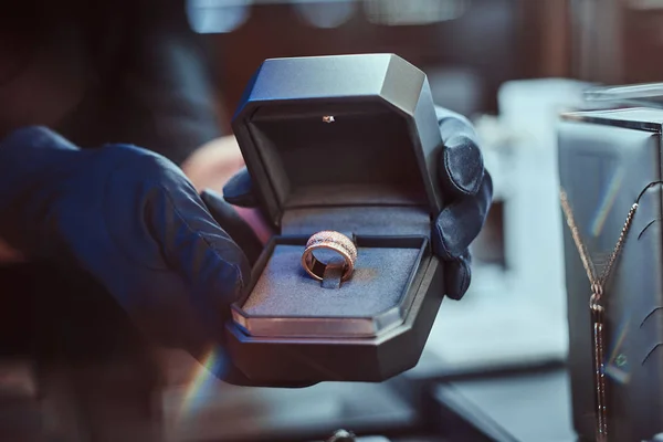 Close-up photo of assistants hands who holds the box with the exclusive gold ring in a jewelry store — Stock Photo, Image