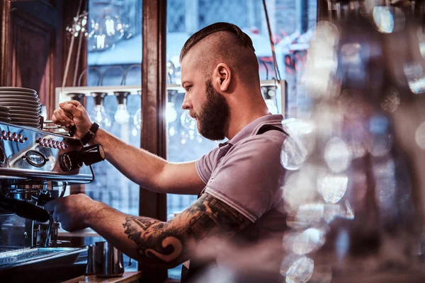 Tattooed barista with stylish beard and hairstyle working on a coffee machine in a coffee shop or restaurant — Stock Photo, Image