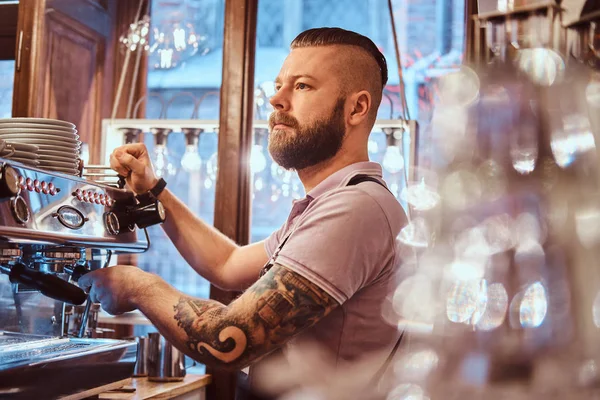 Tattooed barista with stylish beard and hairstyle working on a coffee machine in a coffee shop or restaurant — Stock Photo, Image