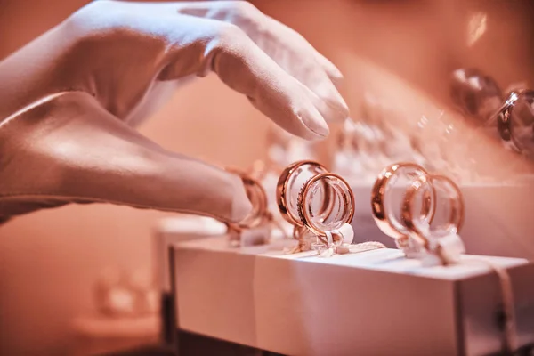 Hand in gloves takes to exclusive rings on the showcase of a jewelry store — Stock Photo, Image