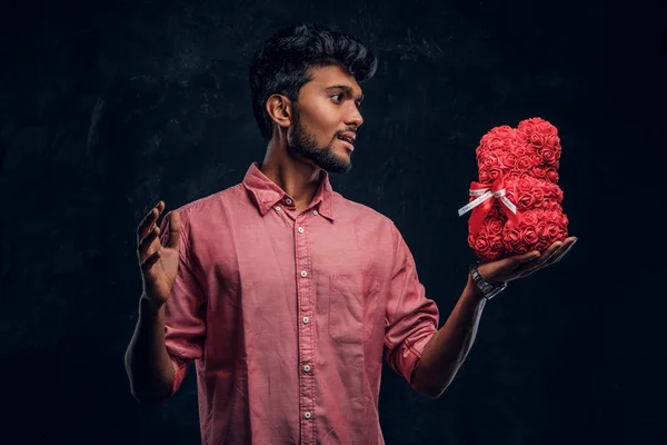 Indiase man in een roze shirt houdt van een mooi cadeau en kijkt hem met een enthousiaste uitstraling. Romantische stemming, liefdesrelatie. — Stockfoto