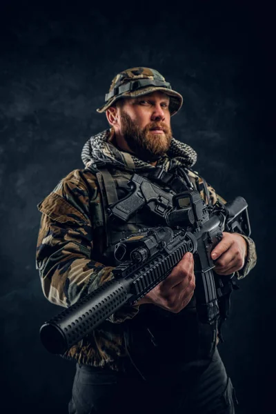 Soldado das forças especiais no uniforme camuflado militar segurando um rifle de assalto. Foto do estúdio contra uma parede de textura escura — Fotografia de Stock