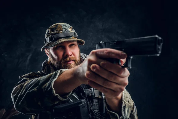 Homem brutal no uniforme camuflado militar segurando uma arma e apontando para o inimigo . — Fotografia de Stock