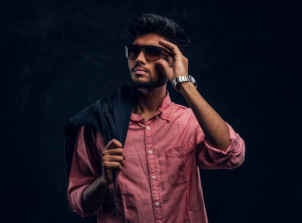 Vogue, fashion, style. Handsome young Indian guy wearing a pink shirt and sunglasses holding a jacket on his shoulder and looking sideways. — 图库照片