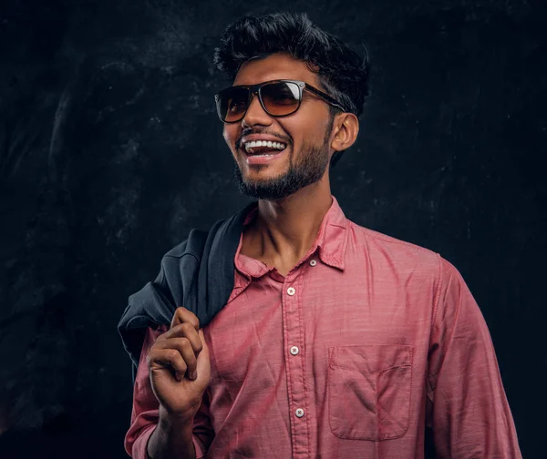 Vogue, moda, stil. Gülümseyen ve yana doğru seyir pembe gömlek ve ceket omzunda, holding güneş gözlüğü takmış yakışıklı genç Hintli adam. — Stok fotoğraf