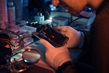 Teknisyen dikkatle smartphone içinde modern bir tamirciye iç unsurları bütünlüğünü inceler