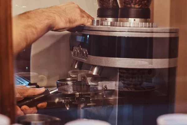 Barista hält einen Portafilter mit schwarzem gemahlenem Kaffee in der Hand und arbeitet an einer Kaffeemaschine in einem Café oder Restaurant — Stockfoto