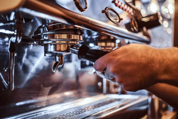 Foto de un barista sosteniendo un portafilter con un café negro molido y trabajando en una máquina de café en una cafetería o restaurante —  Fotos de Stock