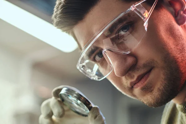 Крупный план электронного техника в очках, держащего увеличительное стекло и смотрящего в камеру — стоковое фото