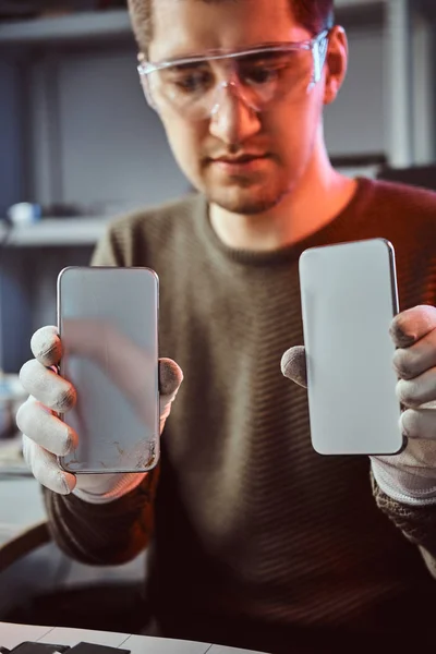 Techniker hält zwei identische Smartphones zum Vergleich, in einer Hand kaputt und in einer anderen neu — Stockfoto
