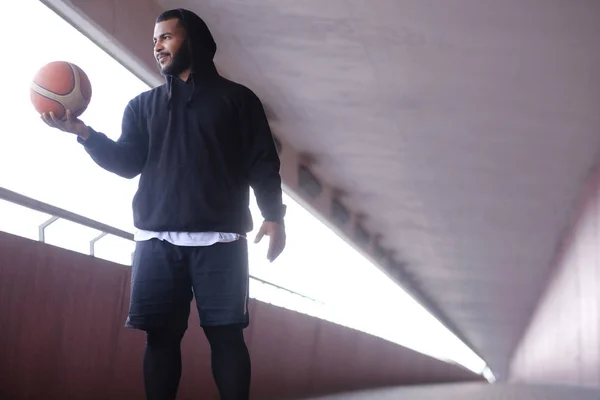 Afrika-Amerika pria mengenakan hoodie hitam memegang bola basket sambil berdiri di jembatan trotoar — Stok Foto