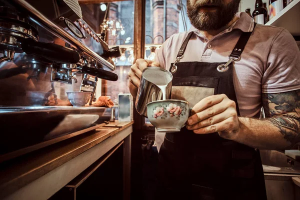 Barista vestindo avental fazendo um cappuccino, derramando leite em uma xícara em um restaurante ou café — Fotografia de Stock