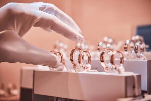 Hand in gloves takes to exclusive rings on the showcase of a jewelry store — Stock Photo, Image