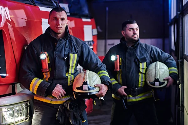 Dva hasiči nosí ochranné jednotný stát vedle hasičské auto v garáži hasiči. — Stock fotografie