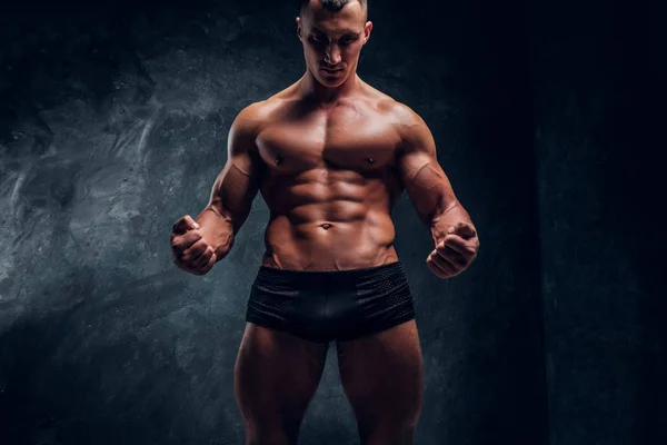 Hombre atlético en ropa interior mostrando su cuerpo bombeado perfecto. Estudio foto con fondo de pared oscura — Foto de Stock