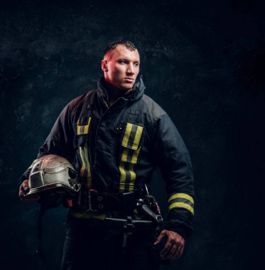 Acımasız itfaiyeci yana görünüyor ve kask elinde tutuyor 