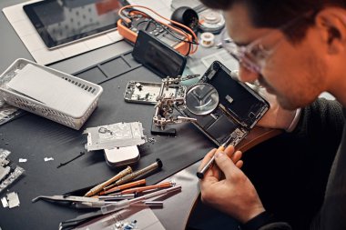 Asker atölye hasarlı smartphone onarmak için Büyüteç'i ve tornavida kullanır.