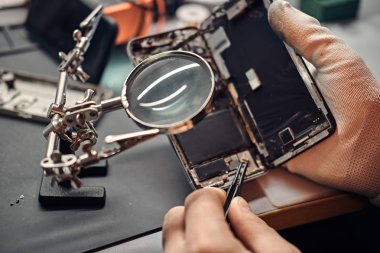Tamirci hasarlı smartphone onarmak için Büyüteç'i ve cımbız kullanır.