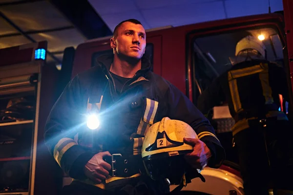 Los bomberos vinieron a la llamada por la noche. Bombero guapo con un uniforme protector con una linterna incluida — Foto de Stock