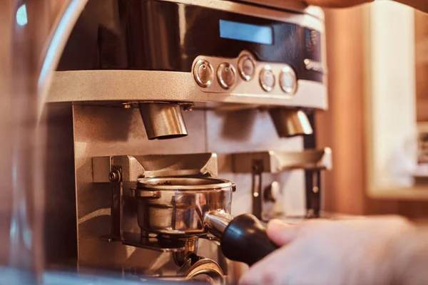 Barista segurando um portafilter com um café moído preto e trabalhando em uma máquina de café em uma cafeteria ou restaurante — Fotografia de Stock