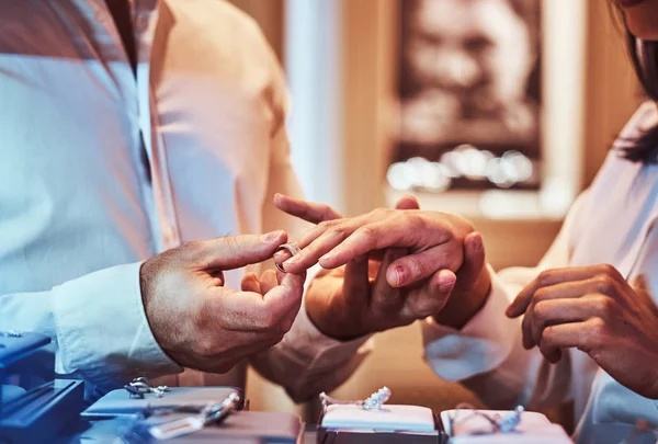 Elegantly dressed man trying on the wedding ring on the hand of his girlfriend in a jewelry store