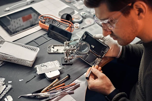 Servicemann repariert beschädigtes Smartphone in der Werkstatt mit Lupe und Schraubenzieher. — Stockfoto