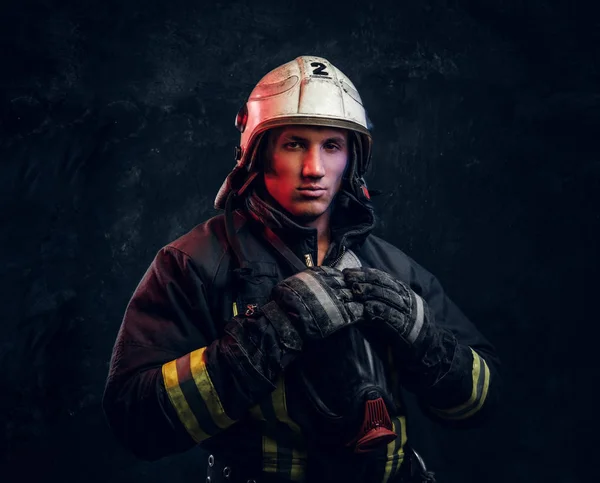 Πυροσβέστης με στολή και ασφάλειας κράνος, θέτοντας σε ένα σκοτεινό στούντιο — Φωτογραφία Αρχείου