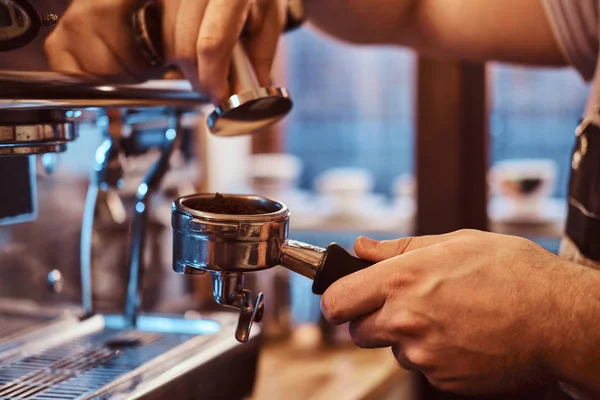 Foto de close-up de uma mão segurando um portafilter com um café moído preto em uma cafeteria ou restaurante — Fotografia de Stock