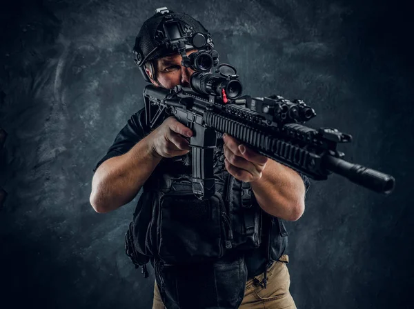 Special forces soldier wearing body armor and helmet with night vision holding an assault rifle. Studio photo against a dark textured wall — Stock Photo, Image