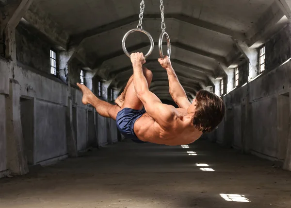 Um atleta profissional com corpo muscular fazendo exercício de ginástica em anéis, mostra a suspensão horizontal no edifício industrial abandonado — Fotografia de Stock