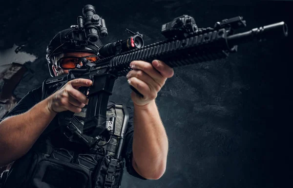 Soldado de las fuerzas especiales con chaleco antibalas y casco con visión nocturna sosteniendo un rifle de asalto. Foto del estudio contra una pared de textura oscura —  Fotos de Stock